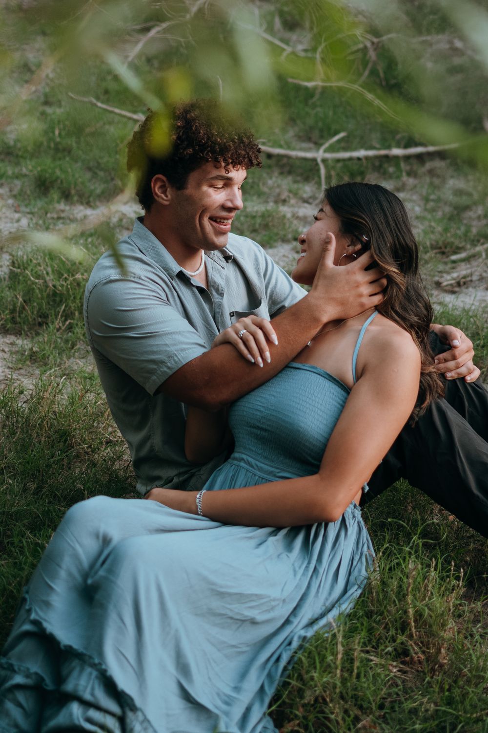 A couple shares a tender moment while sitting together in nature wearing coordinating blue outfits.