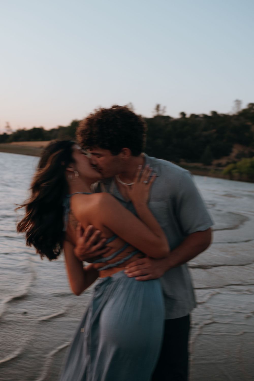 A couple shares romantic moments by the water at sunset in a series of candid photos.