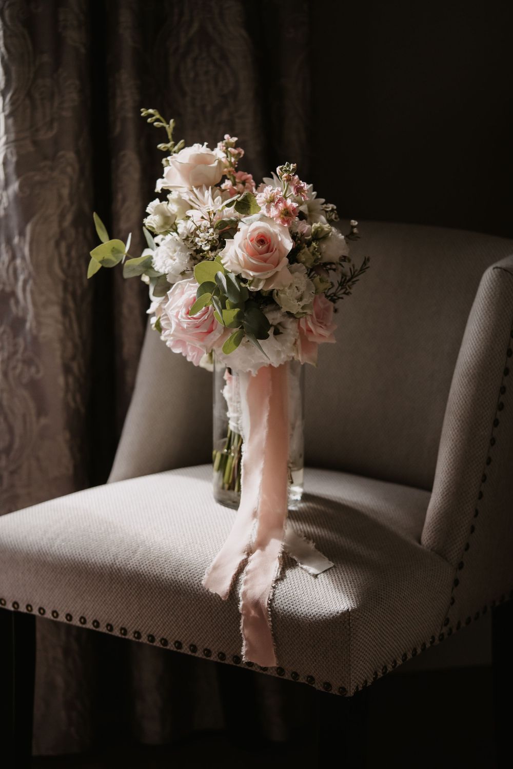 Elegant bridal bouquet with pink and white roses resting on a gray upholstered chair.