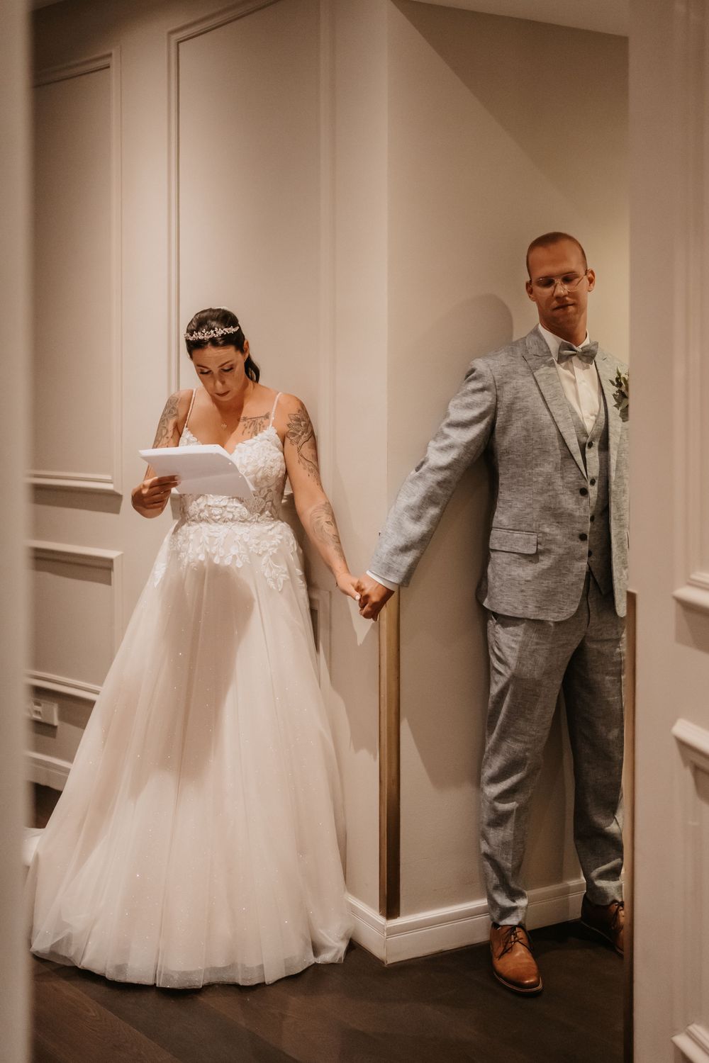Bride and groom share first look moment while separated by a wall corner.