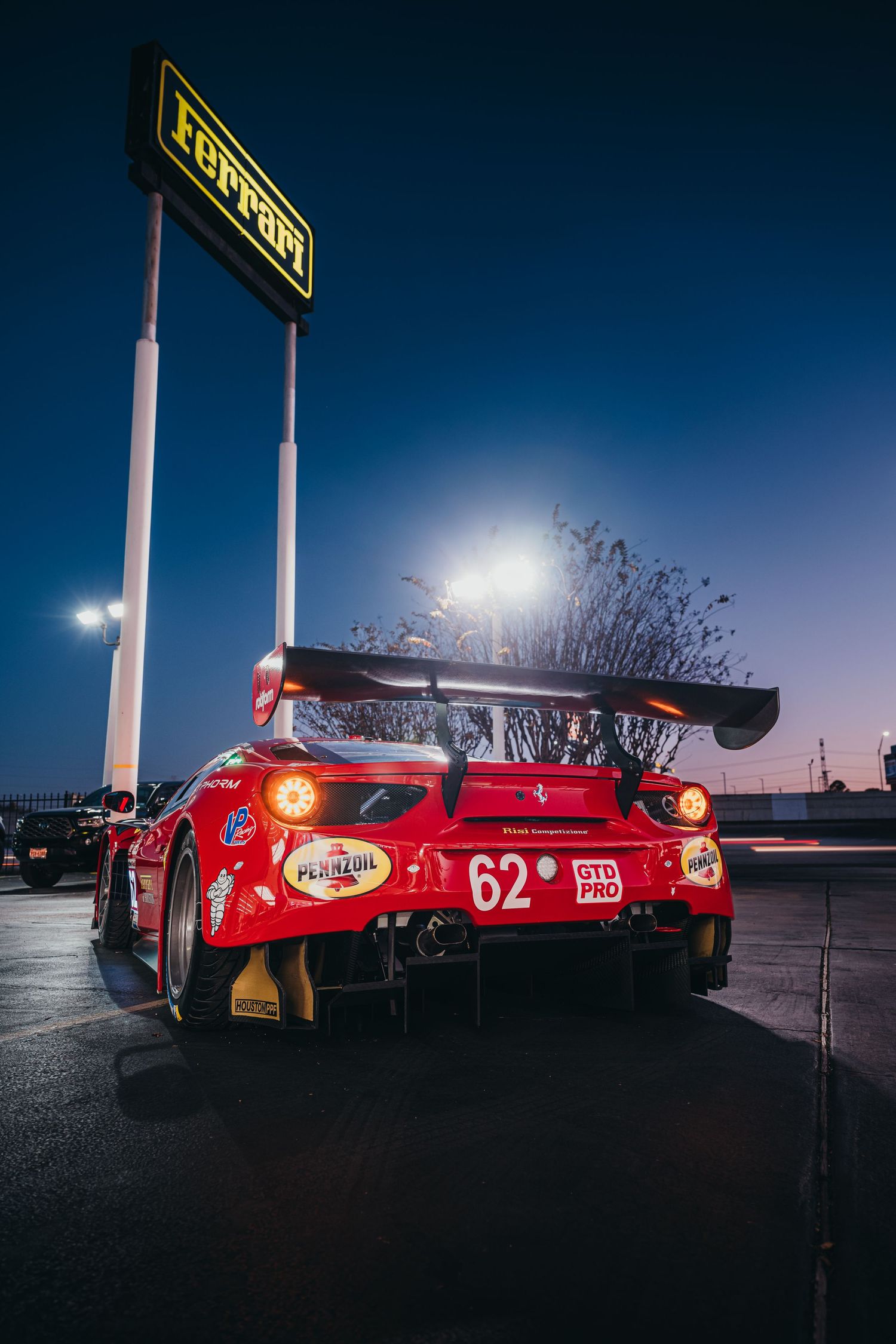 Red Ferrari race car photographed at dusk with stadium lights creating dramatic silhouette.