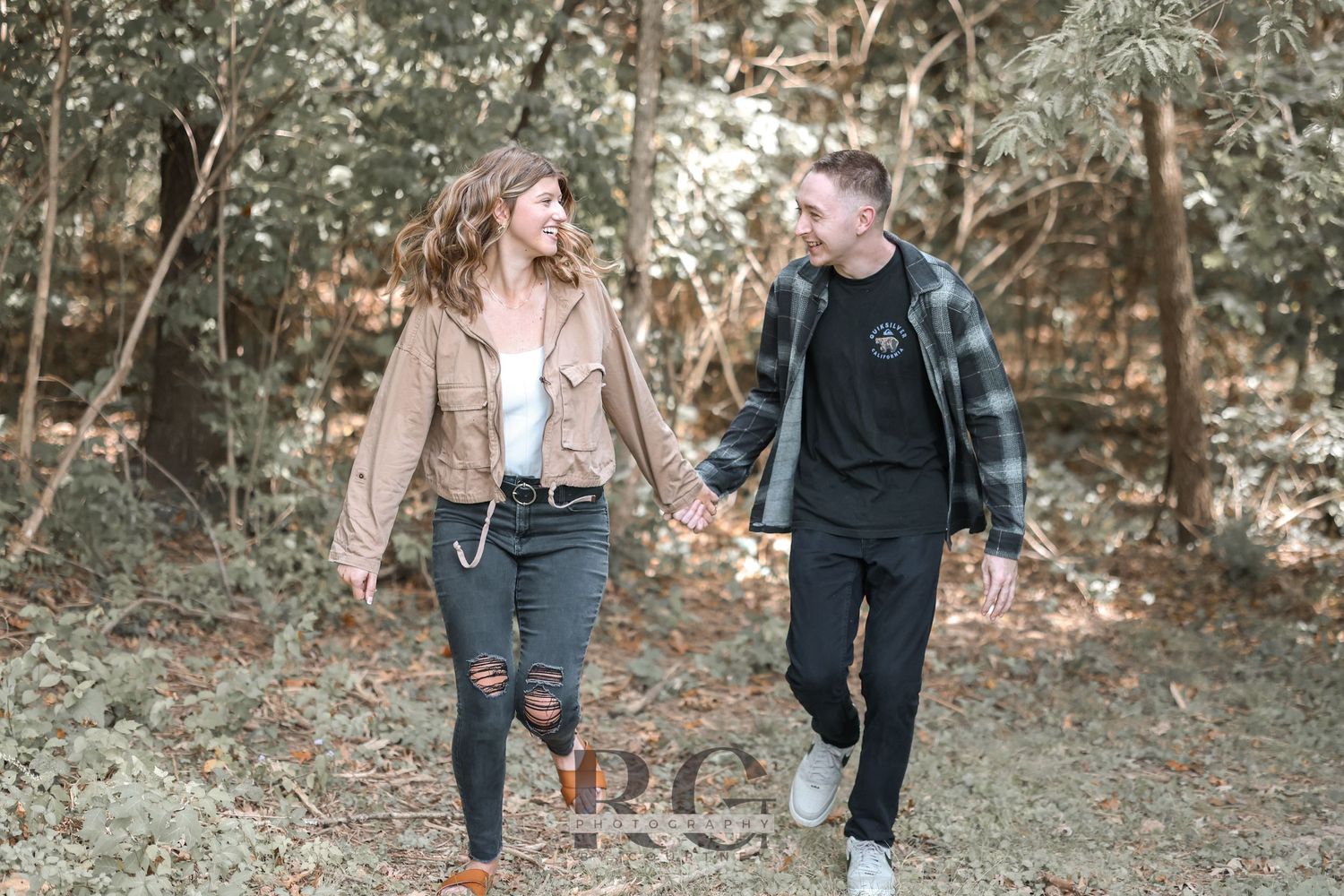 A couple walks together through autumn woods holding hands.