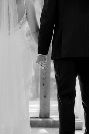 Black and white wedding photo showing the bottom half of a bride in white dress and groom in dark suit standing together.