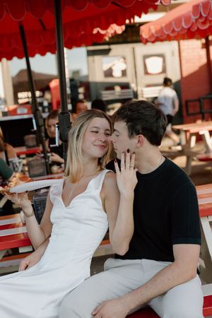 A couple shares an intimate moment while sitting at an outdoor restaurant with red awning overhead.