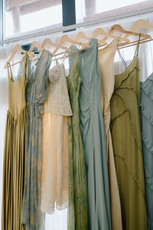 A collection of vintage-style bridesmaid dresses in soft sage green and cream colors hanging on wooden hangers.