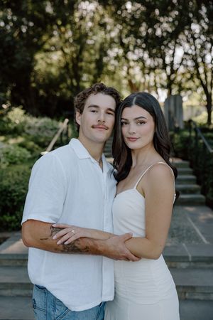 A couple in coordinating white outfits embrace and pose together outdoors during a romantic photoshoot.