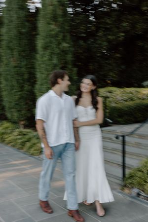 A couple in casual attire dances together on a stone patio surrounded by greenery in a romantic outdoor setting.