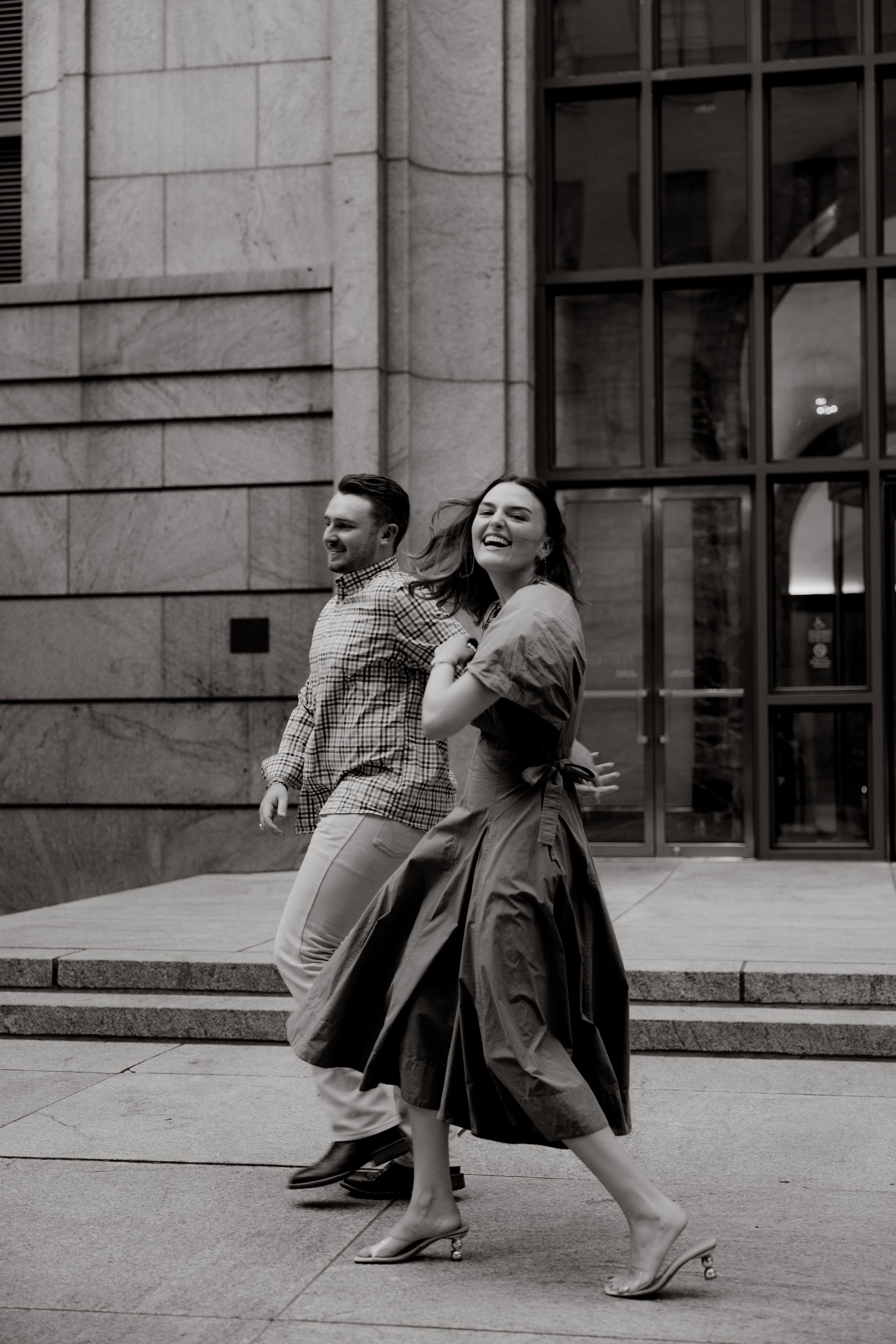 A playful couple dancing and laughing together outside a modern building.