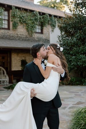 A romantic dip kiss sequence between a couple in formal wedding attire outside a stone building.
