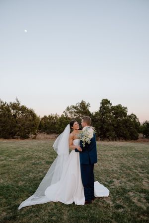 Wedding couple shares a romantic moment in an open field during golden hour with trees in the background.