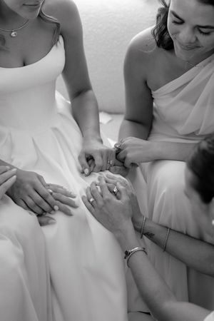 Close-up black and white sequence showing hands adjusting details on a white wedding dress.