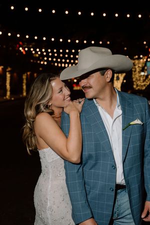 A couple shares a romantic moment at a wedding reception under twinkling string lights.
