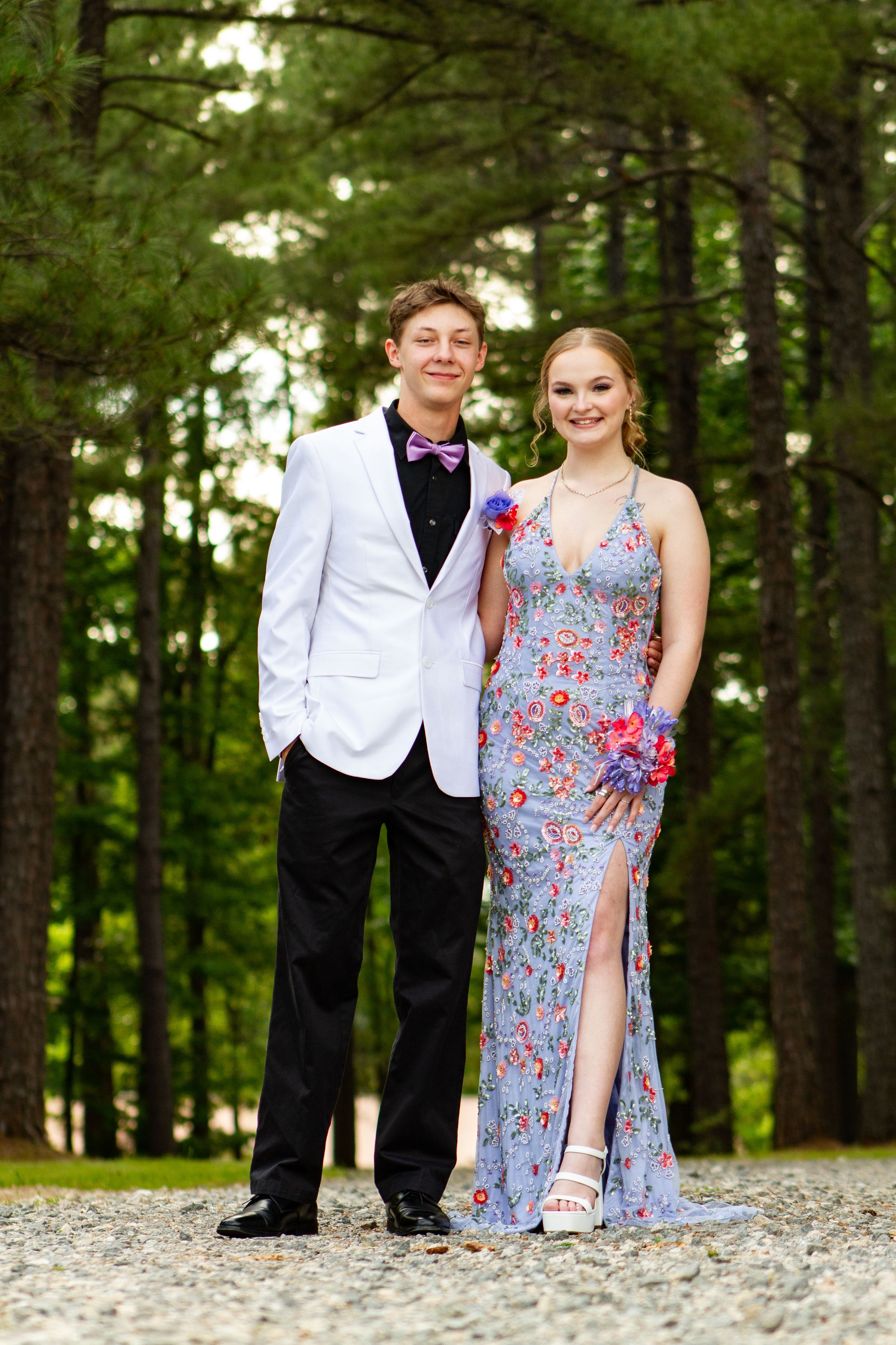 Formal couple standing on gravel path with pine forest background.