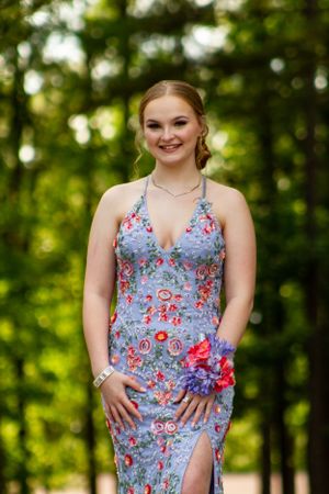 Woman in blue floral prom dress posing against green foliage.