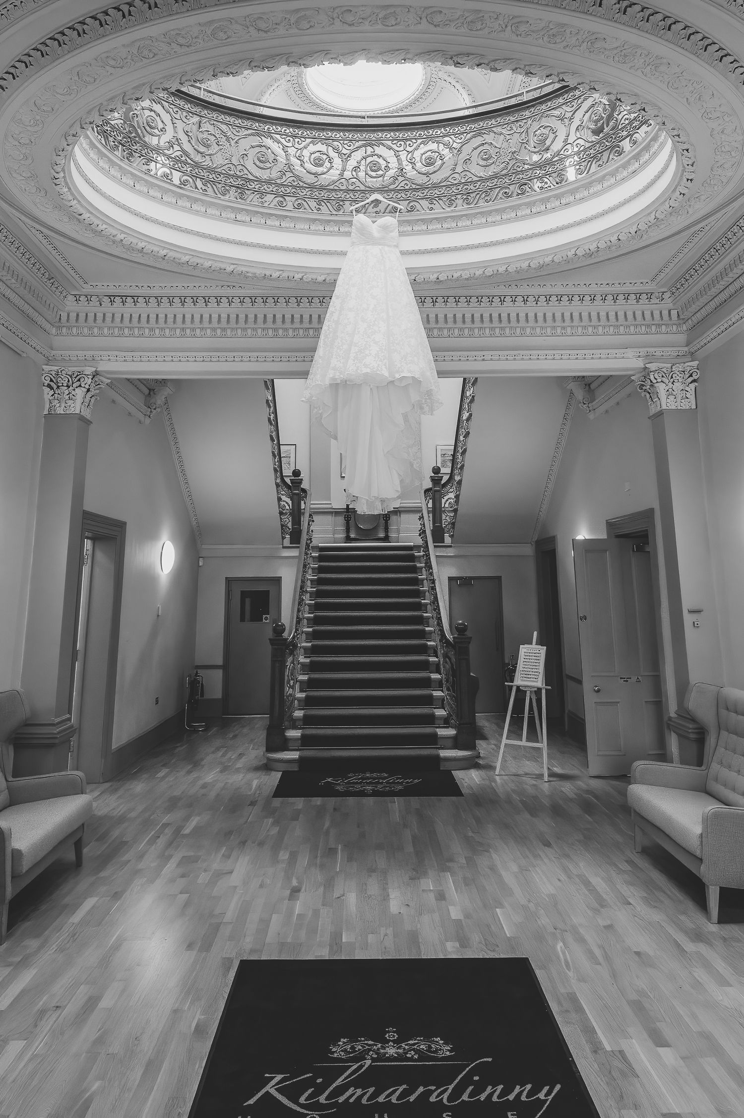 Elegant black and white interior shots of a historic building featuring ornate ceiling details and grand staircases. Wedding dress hanging