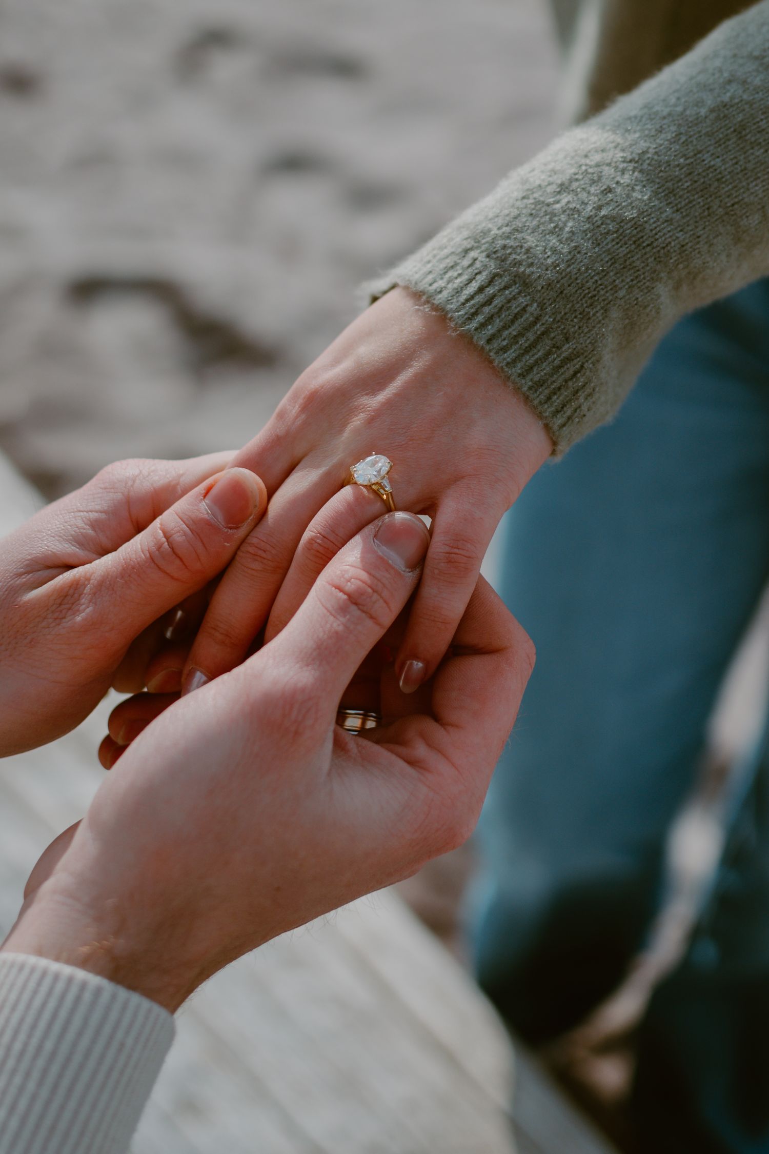 Close-up shot of hands exchanging a diamond engagement ring during a beachside proposal moment.