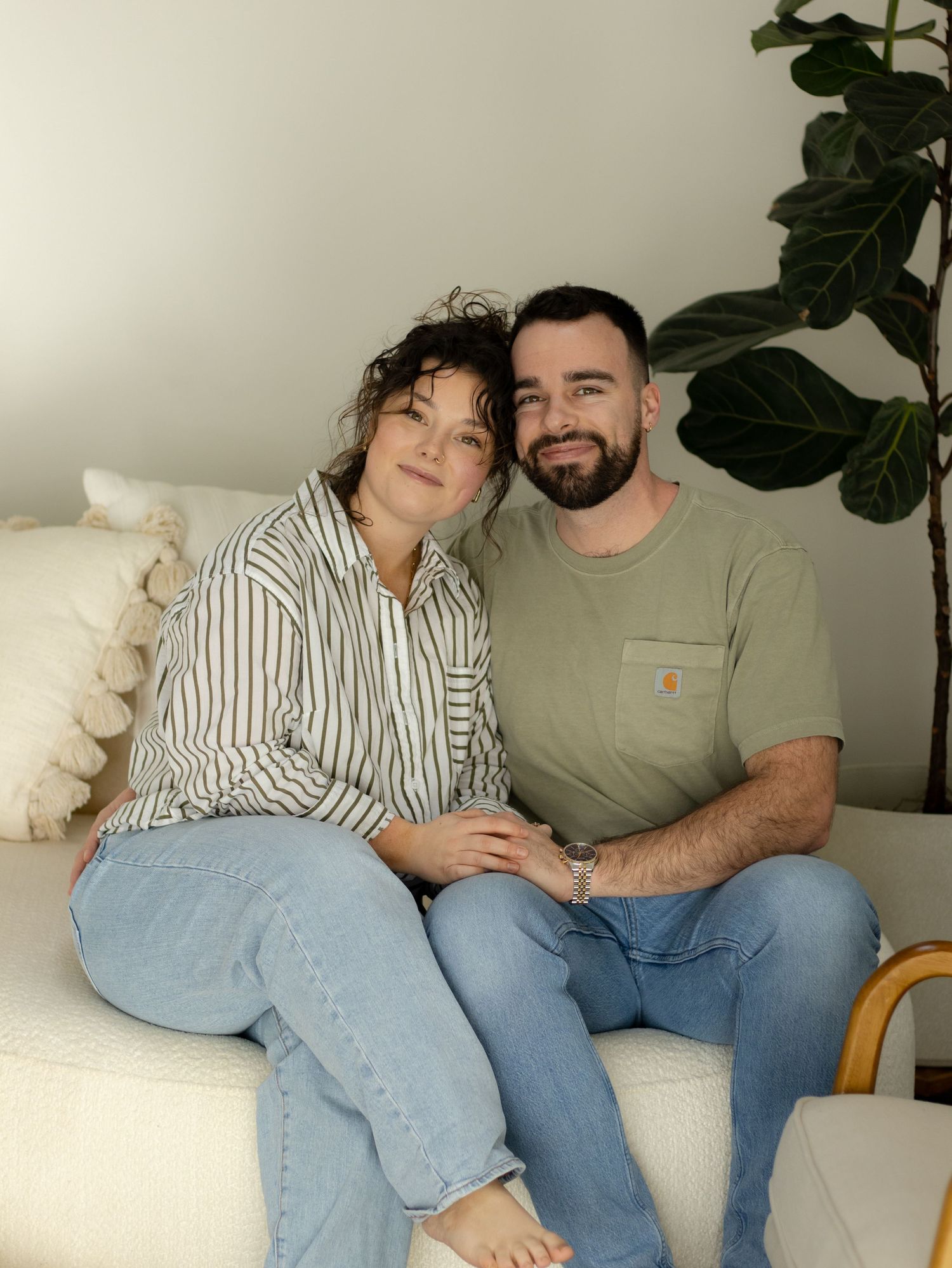 Couple relaxing together on a white couch with a fiddle leaf fig plant in the background.