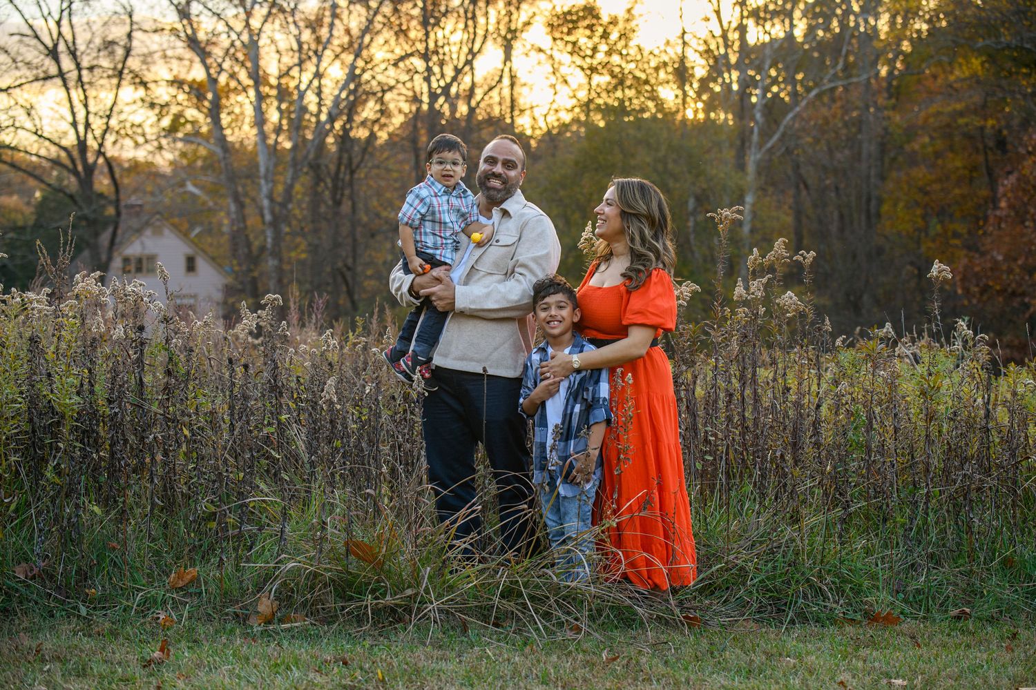 Family photo session at sunset in a natural field setting with tall grass and autumn colors.