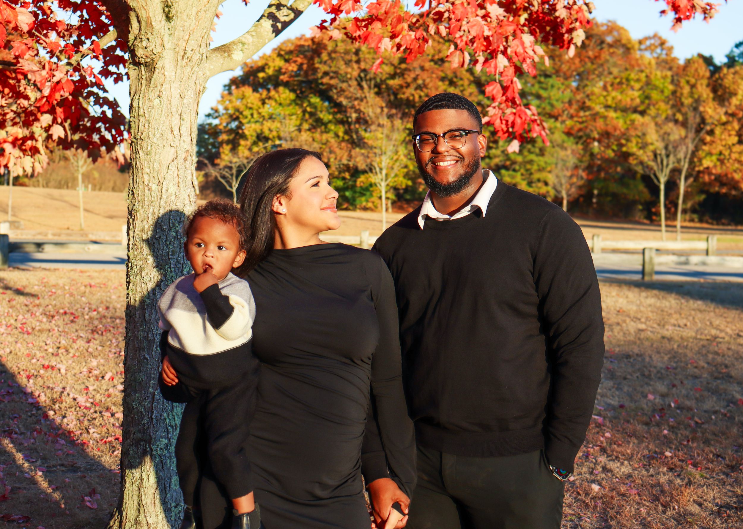 A family smiles together outdoors with vibrant red fall leaves in the background.