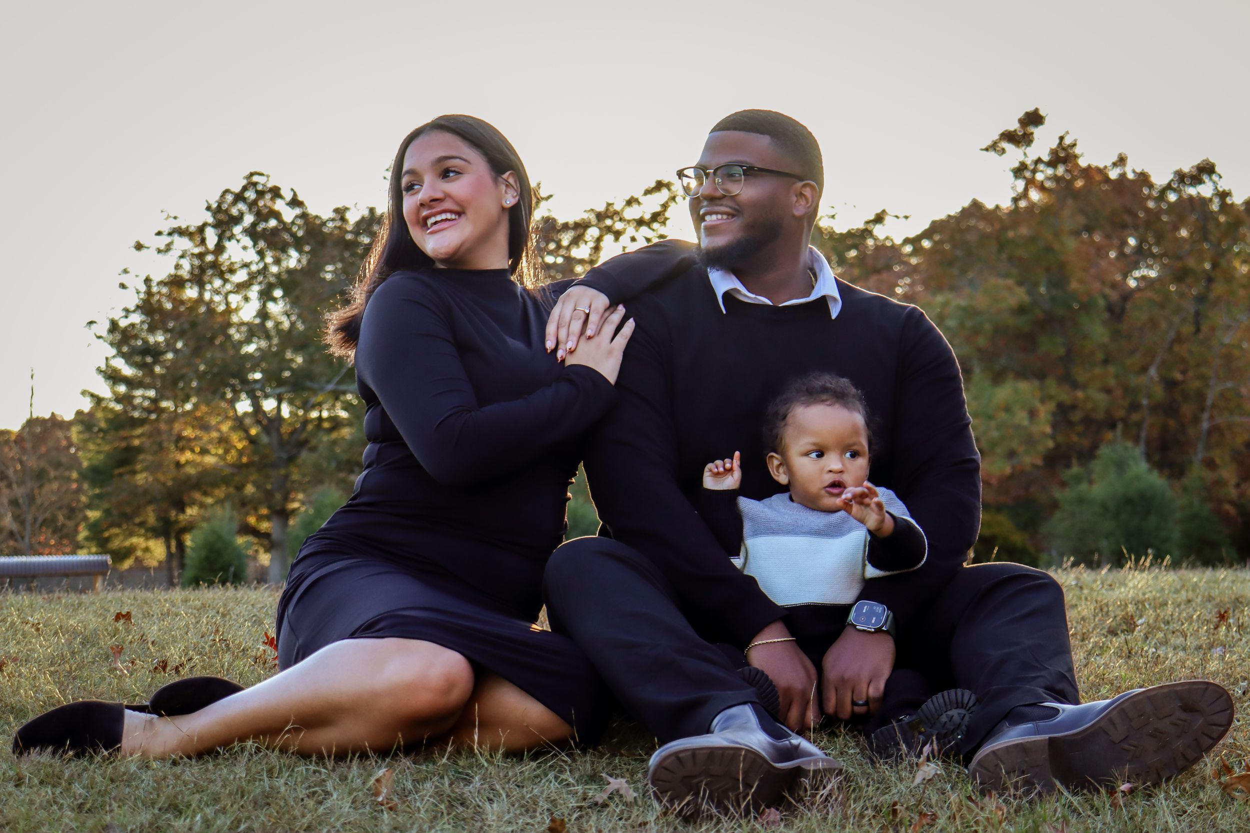 A family poses casually together on grass during an outdoor photo session.