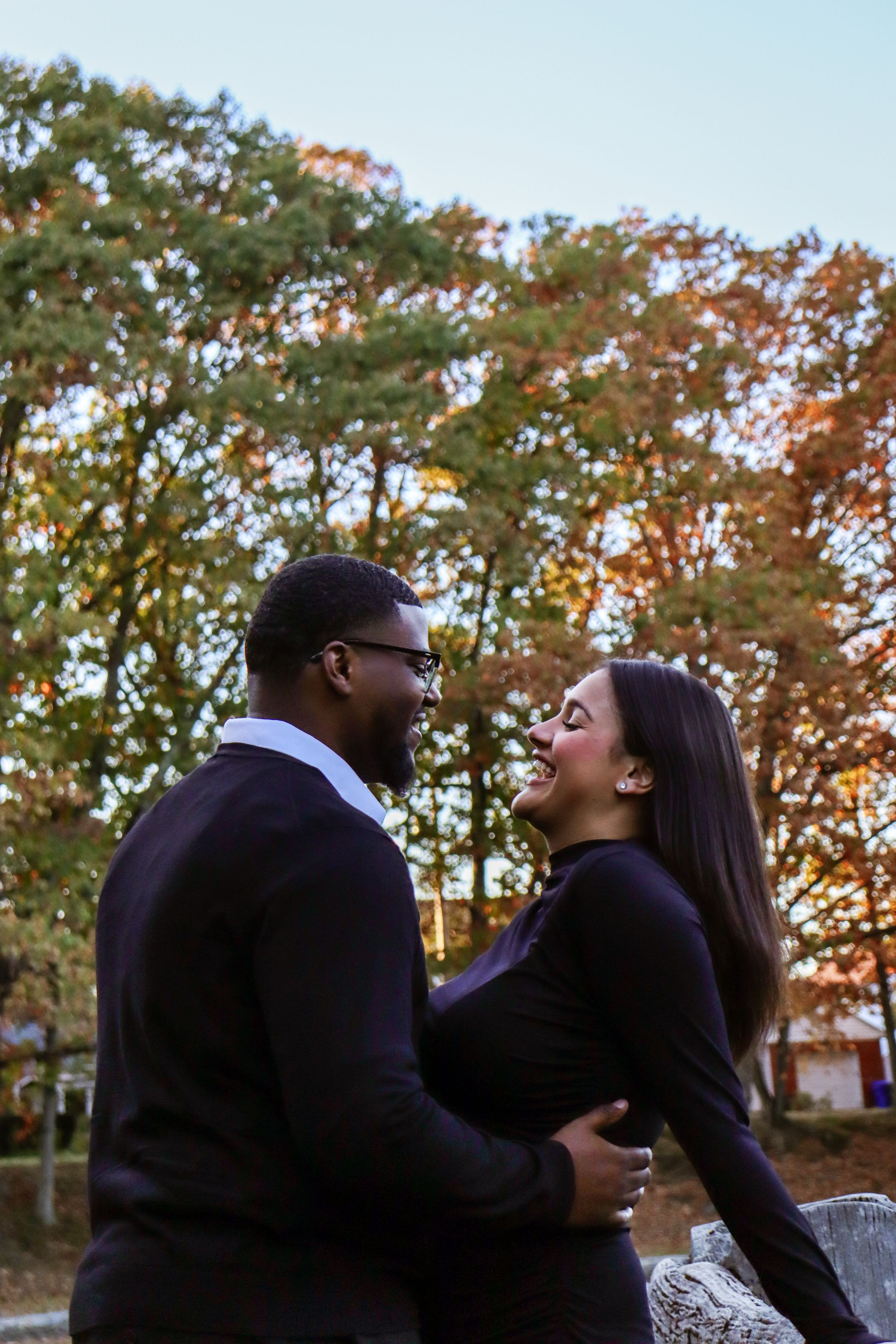 A couple shares a romantic moment outdoors with autumn foliage behind them.