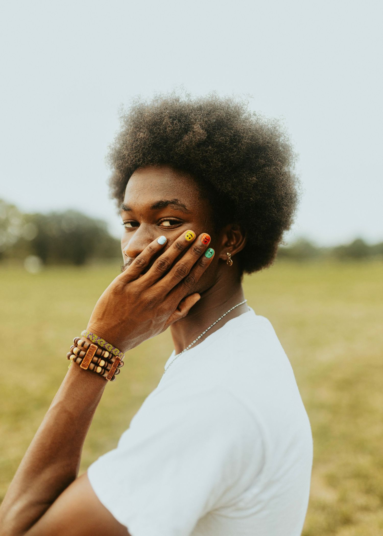 Person in white t-shirt with natural afro hair and jewelry poses in outdoor portrait.