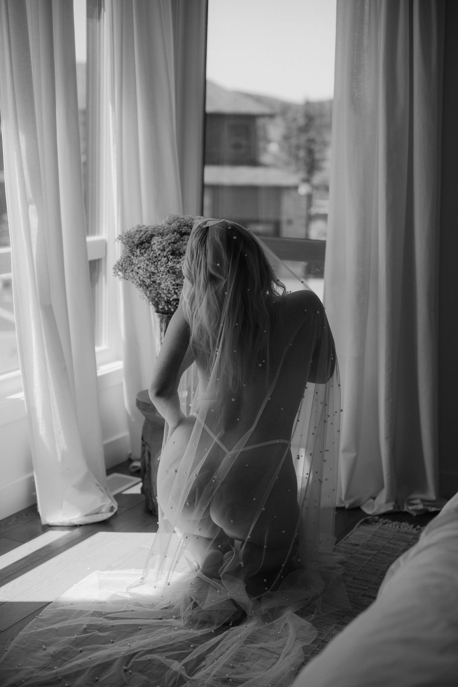 Silhouette of person in wedding dress looking through window with flowing curtains.