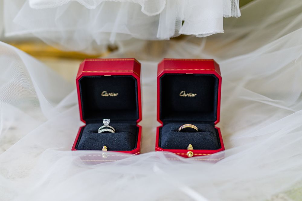 Two red Cartier ring boxes containing wedding bands on white fabric.