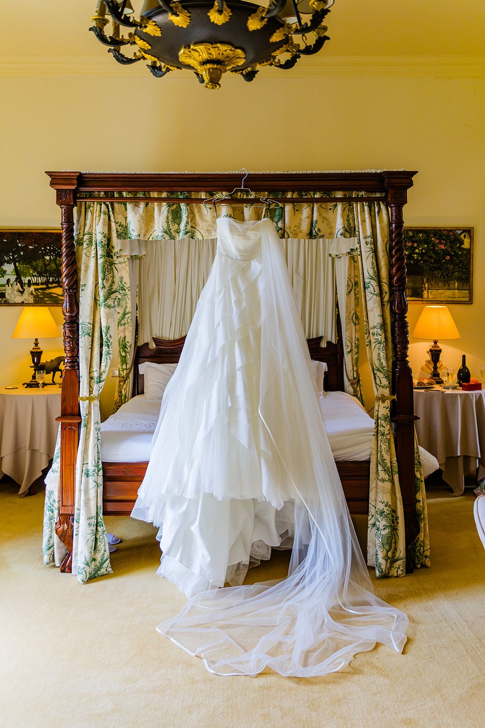 White wedding dress hanging from canopy bed with floral curtains and long flowing train.