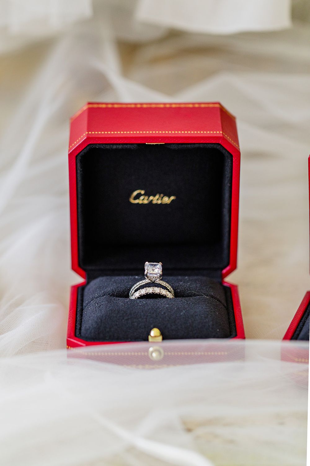 A diamond engagement ring displayed in a red Cartier box on white silk fabric.
