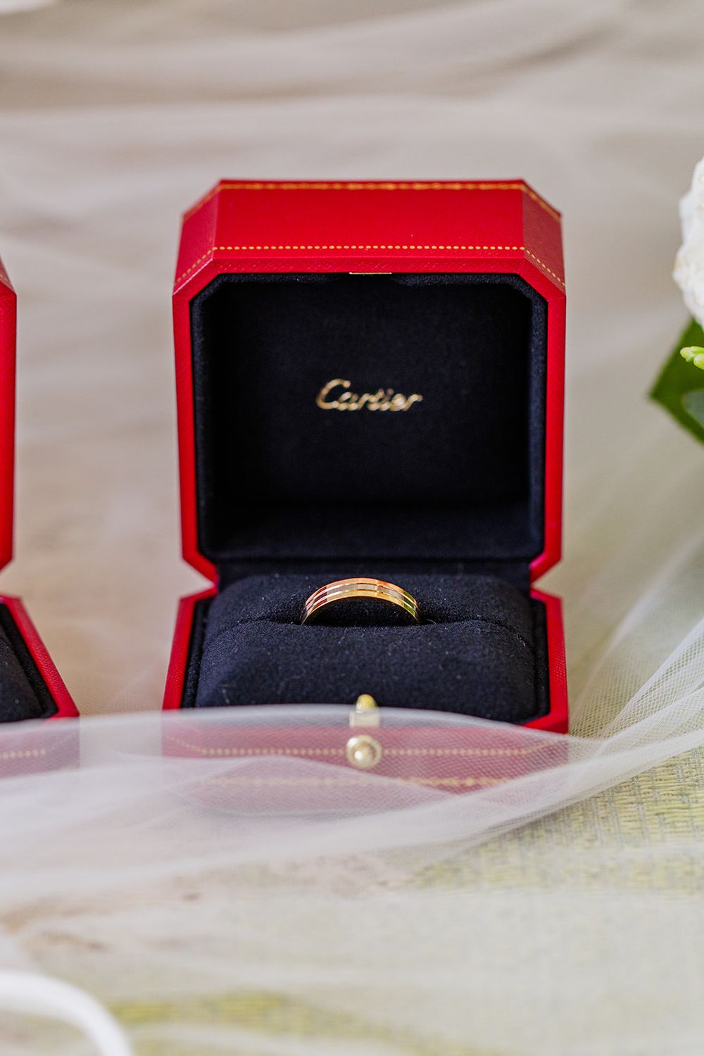 A gold wedding band nestled in a red Cartier ring box on white fabric.