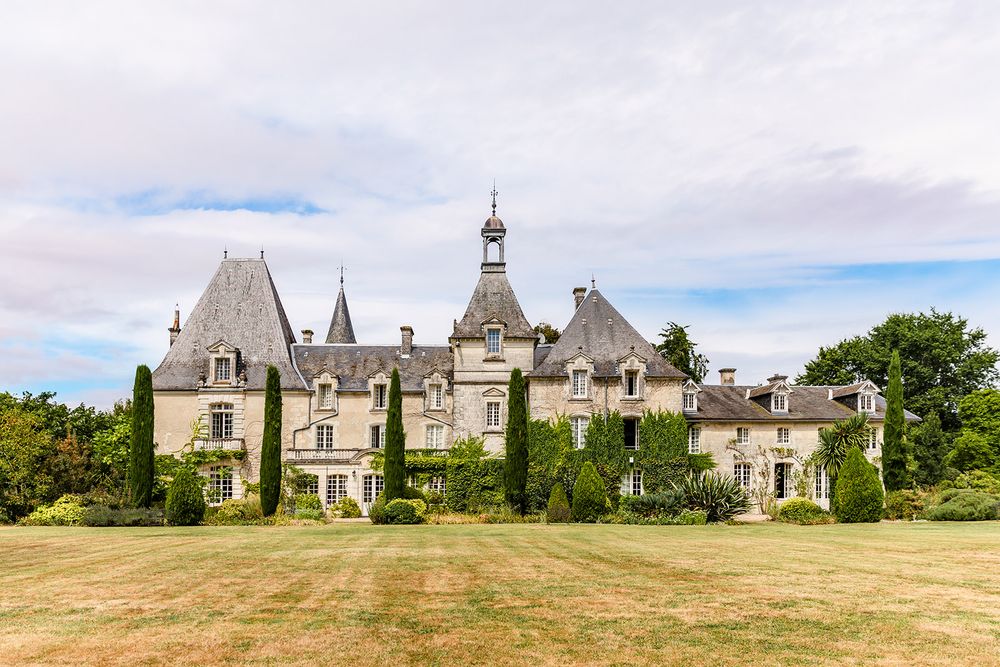 A grand French chateau with gothic architecture and pointed towers against a cloudy sky.