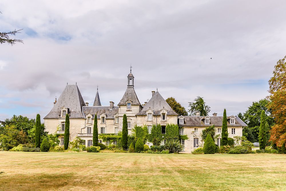 Historic stone chateau with multiple towers and spires surrounded by manicured grounds.