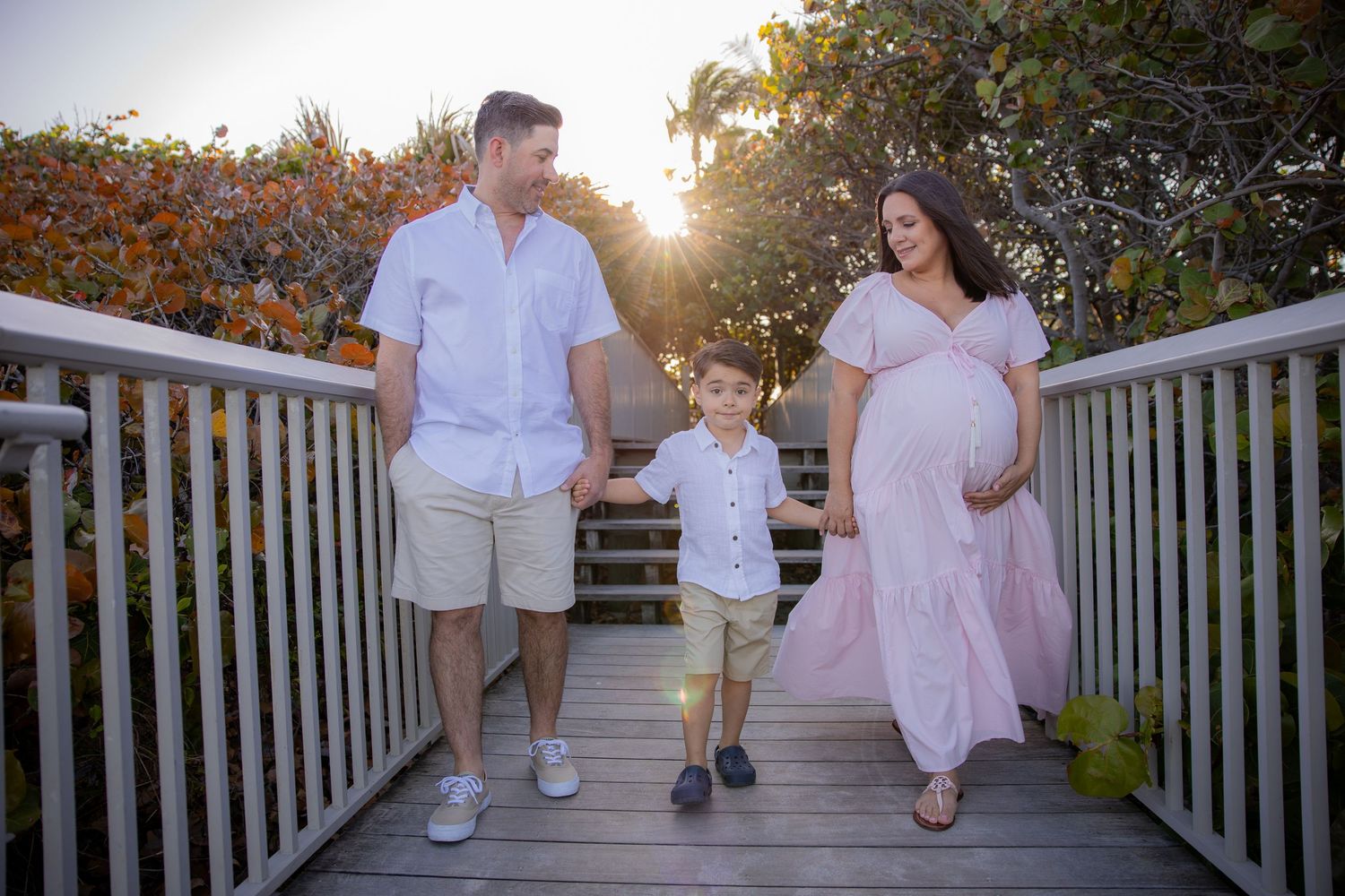 Family holding hands on beach boardwalk with sun flare behind them in Boynton Beach