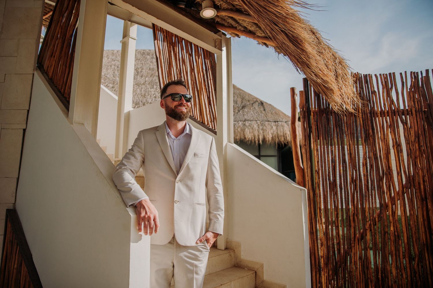 A groom in a light colored suit stands in a rustic outdoor setting Dreams Sapphire Riviera Maya Wedding Photography