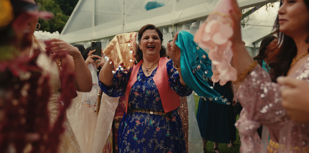 A group of people dancing and celebrating at an outdoor wedding reception under a white tent.