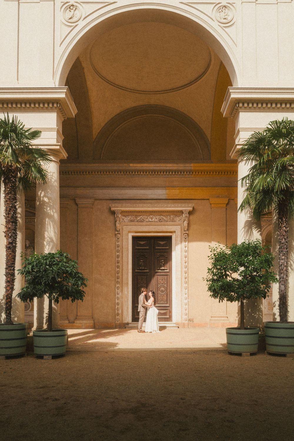 Panoramic view of an elegant arched colonnade with palm trees and green planters in a Mediterranean-style courtyard.