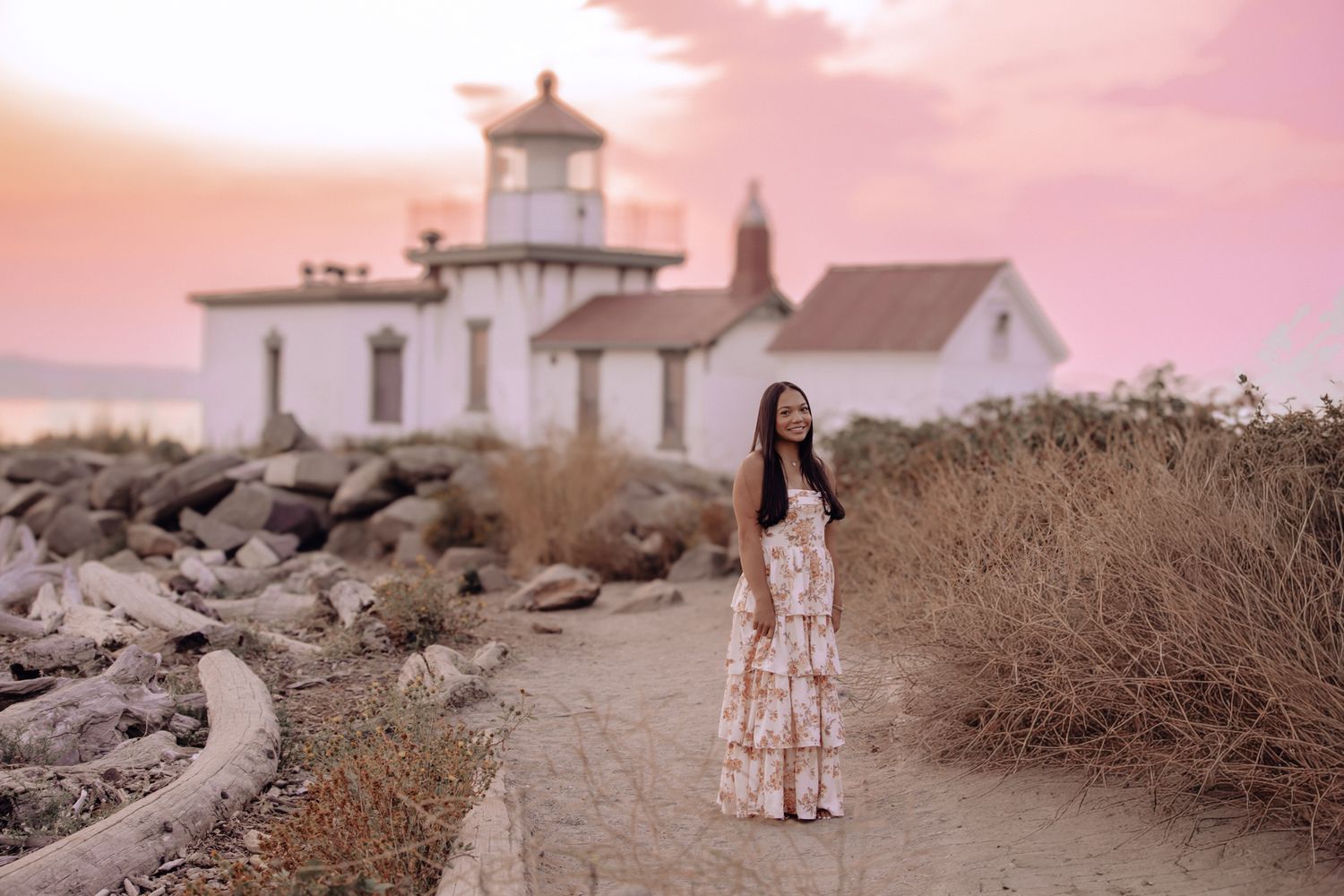 Lighthouse and coastal path at sunset with warm pink sky and seagrass along the trail.