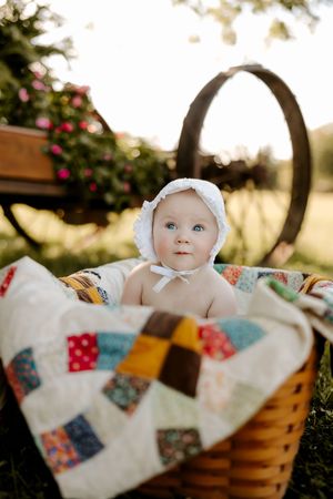 A vintage wicker basket holds a colorful patchwork quilt in a sunny outdoor setting.