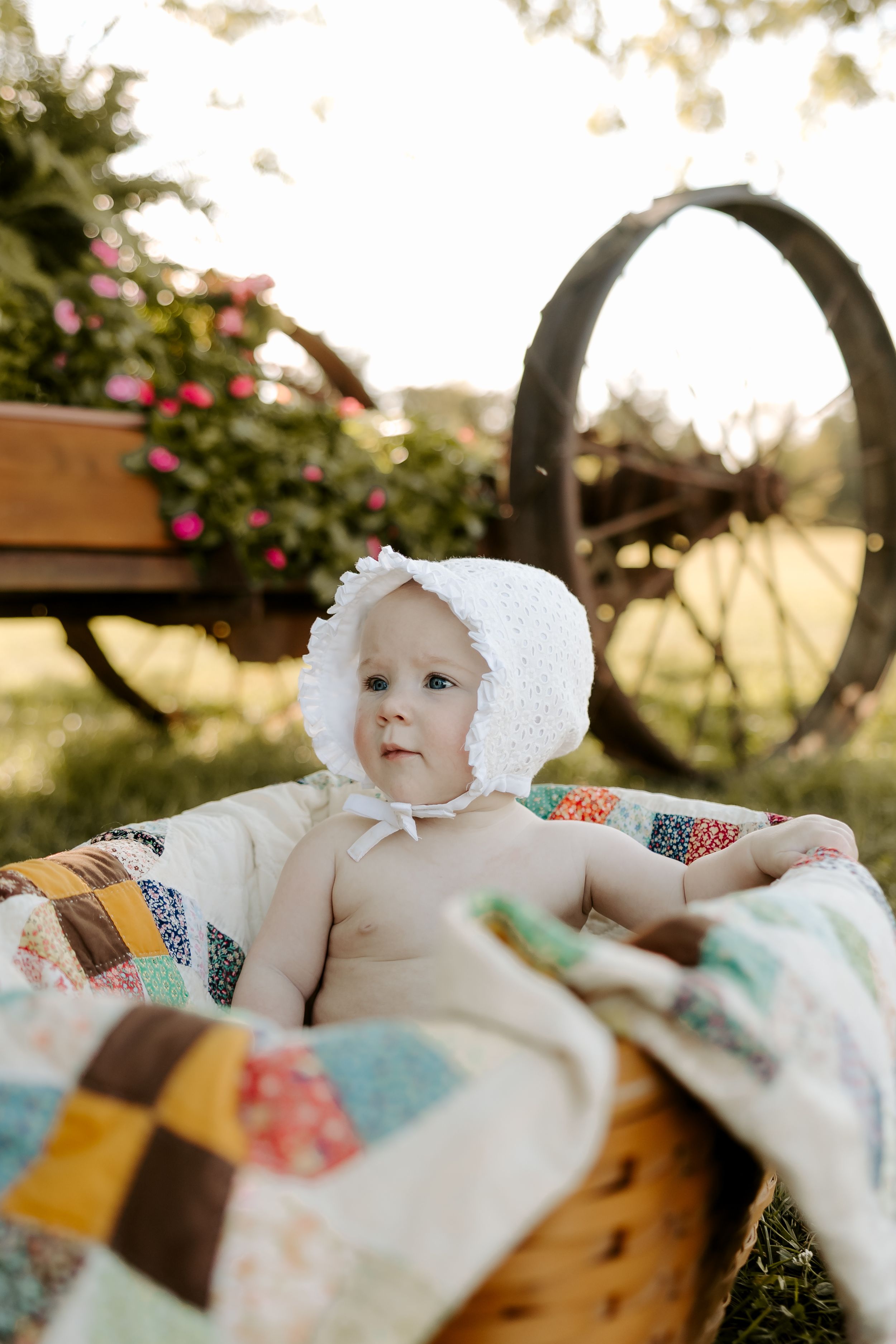 Baby lying on colorful patchwork quilt outdoors during golden hour.