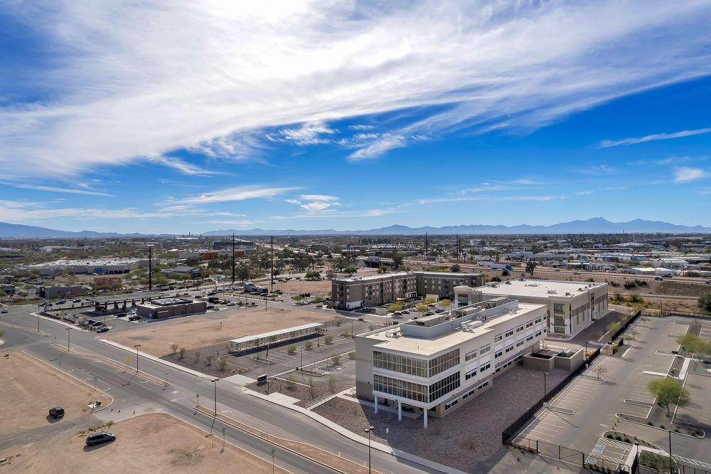 Aerial panoramic view of commercial buildings and parking lots in a desert landscape under bright blue skies.