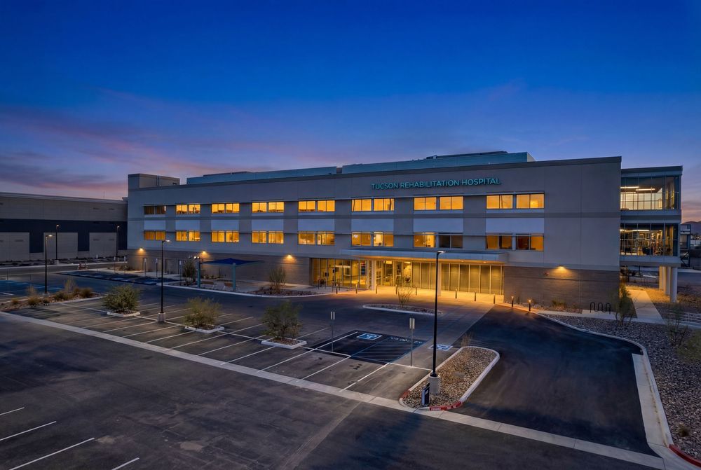Modern commercial building exterior with illuminated windows at dusk and empty parking lot.