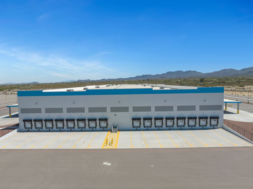 A series of loading docks at a modern industrial warehouse facility with blue sky and mountains in the background.