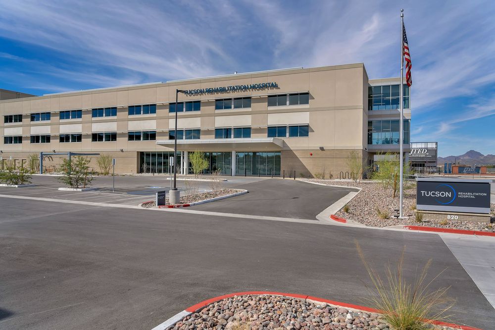 Modern commercial office building exterior with glass windows and landscaping under bright blue sky.