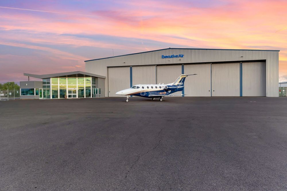 Panoramic view of an airport hangar and runway during a vibrant pink and purple sunset.