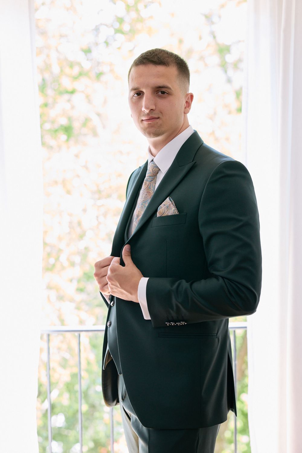 Groom in formal black suit adjusting his tie while getting ready.