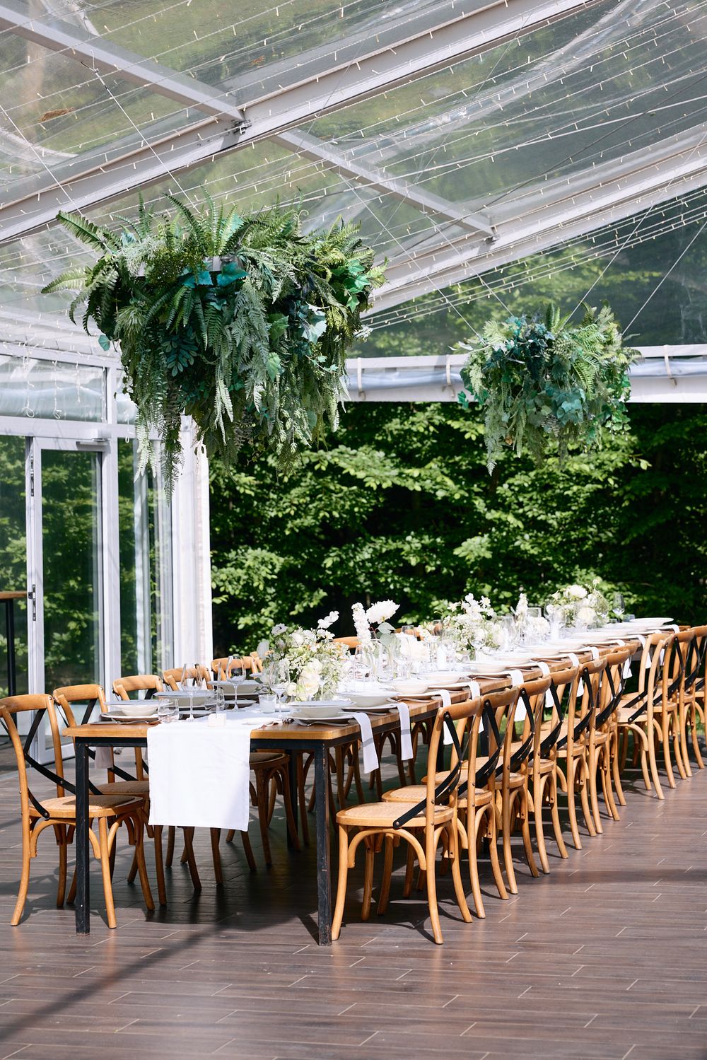 Clear-top tent wedding reception setup with wooden cross-back chairs and elegant table arrangements.