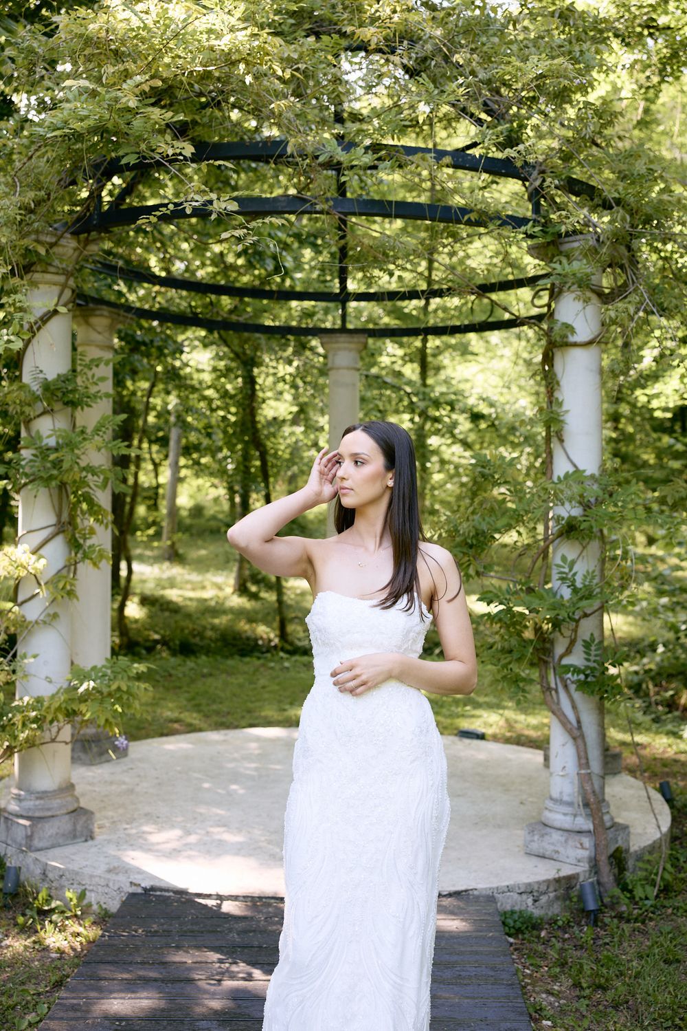 White gazebo in a sunlit garden setting decorated with hanging lanterns and floral elements.