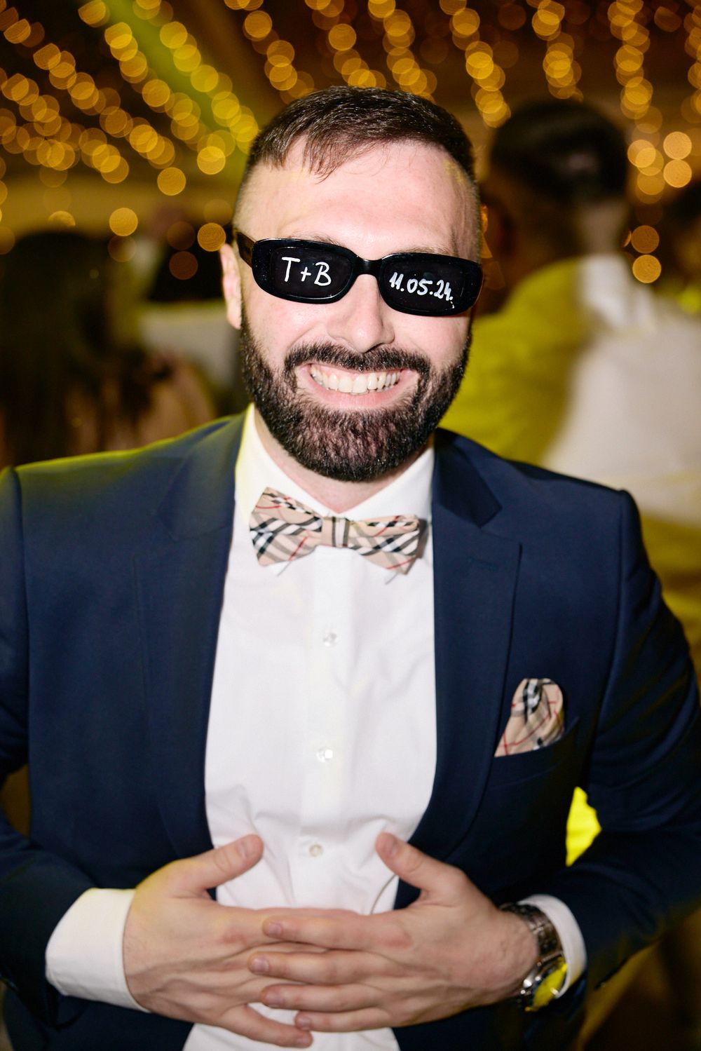 A formal bowtie and navy suit detail with string lights in the background.