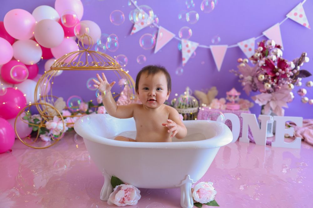 Newborn girl in the bath at the end of her messy cake smash she is enjoying a bubble bath to clean off. princess bathtub.